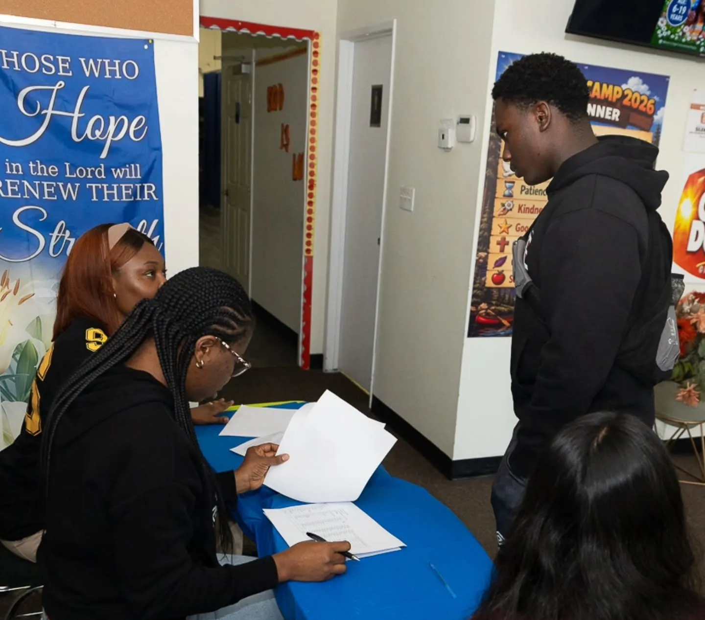 Two volunteers at the welcome desk signing in a young man as he arrives