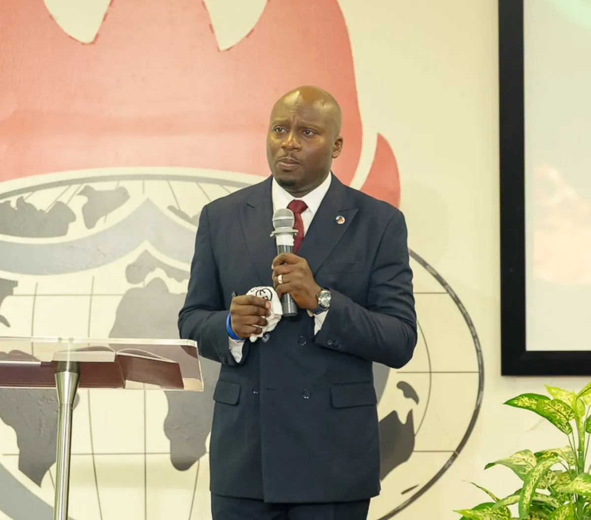 Pastor Adekunle Ogun, Resident Pastor of Winners' Chapel International Regina, in a navy suit holding a microphone